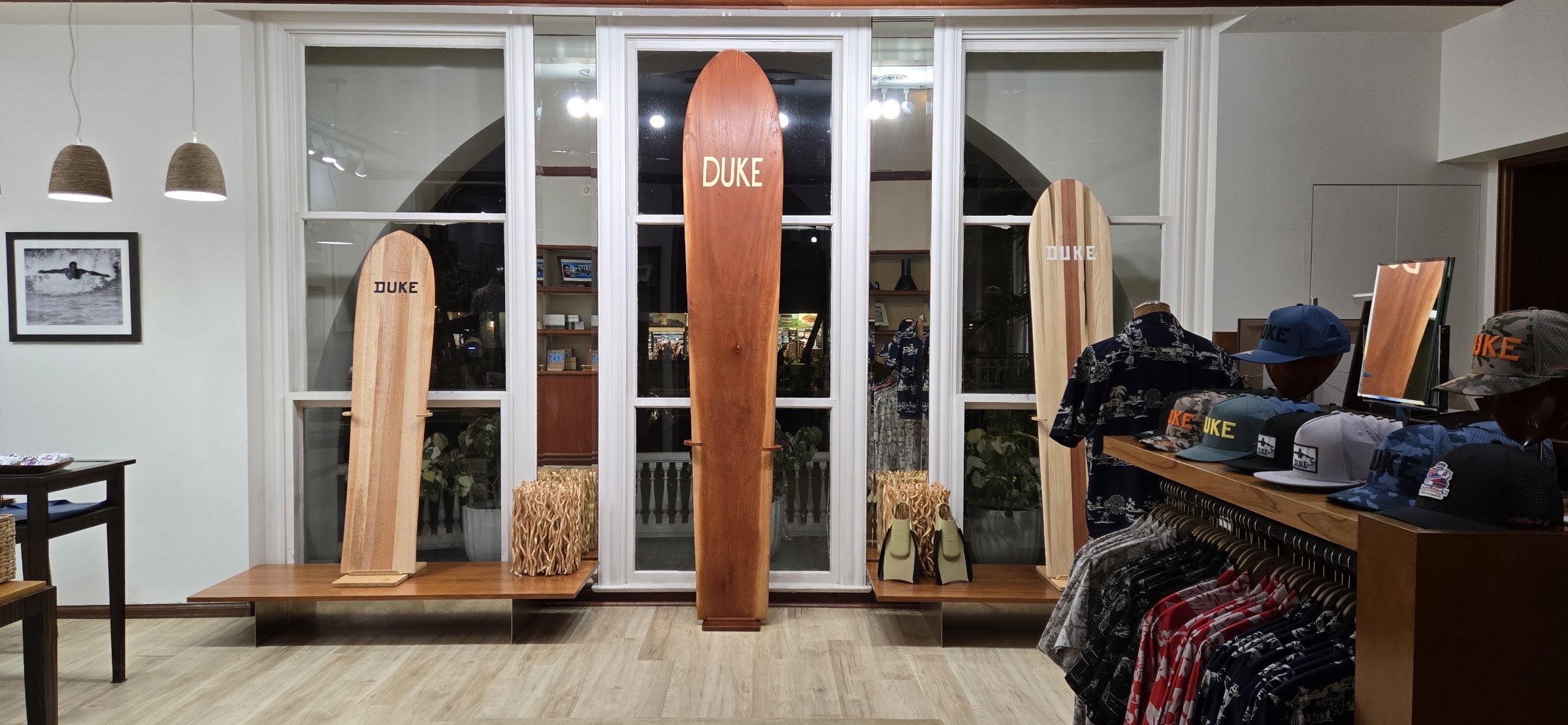 Wooden surfboards standing upright in a bay of tall arched windows with white shutters.